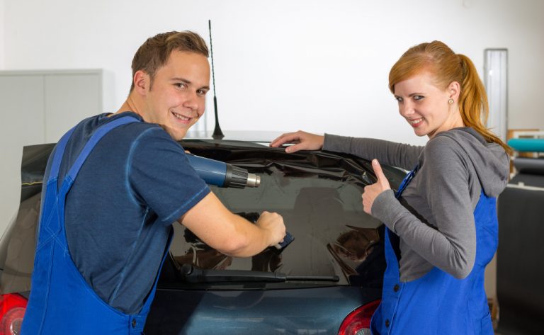 Car wrappers tinting a vehicle window with a tinted foil or film using heat gun and squeegee